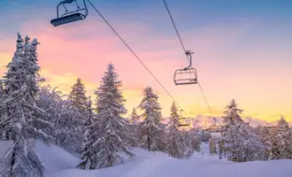 Snowy ski lift at sunrise surrounded by pine trees, representing the winter setting of the Murder on the Slopes virtual team building game in Ireland.