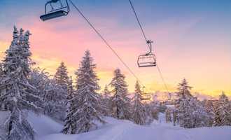 Snowy ski lift at sunrise surrounded by pine trees, representing the winter setting of the Murder on the Slopes virtual team building game in Ireland.