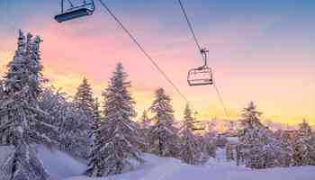 Snowy ski lift at sunrise surrounded by pine trees, representing the winter setting of the Murder on the Slopes virtual team building game in Ireland.
