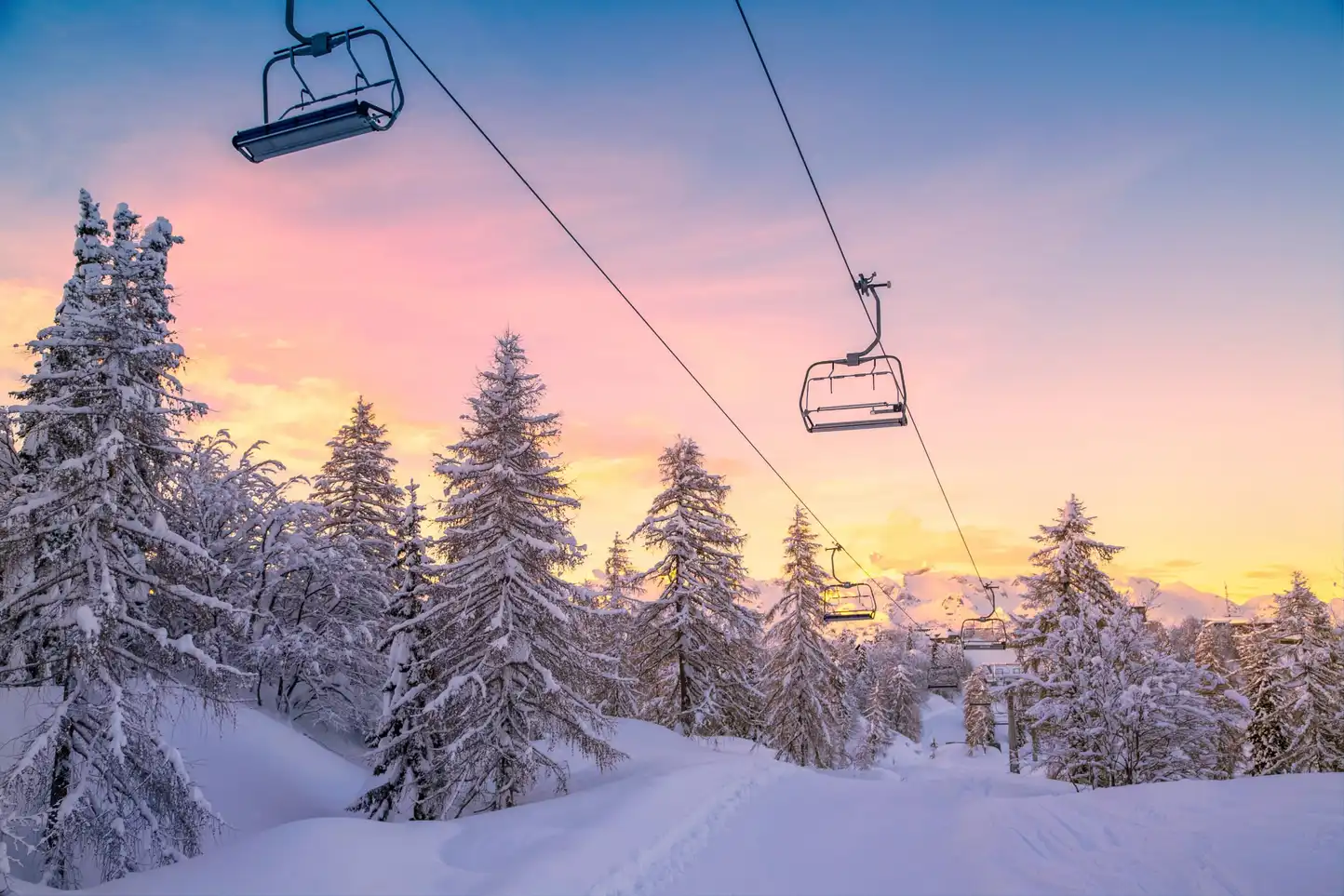 Snowy ski lift at sunrise surrounded by pine trees, representing the winter setting of the Murder on the Slopes virtual team building game in Ireland.