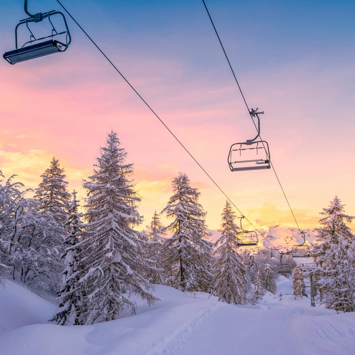 Snowy ski lift at sunrise surrounded by pine trees, representing the winter setting of the Murder on the Slopes virtual team building game in Ireland.