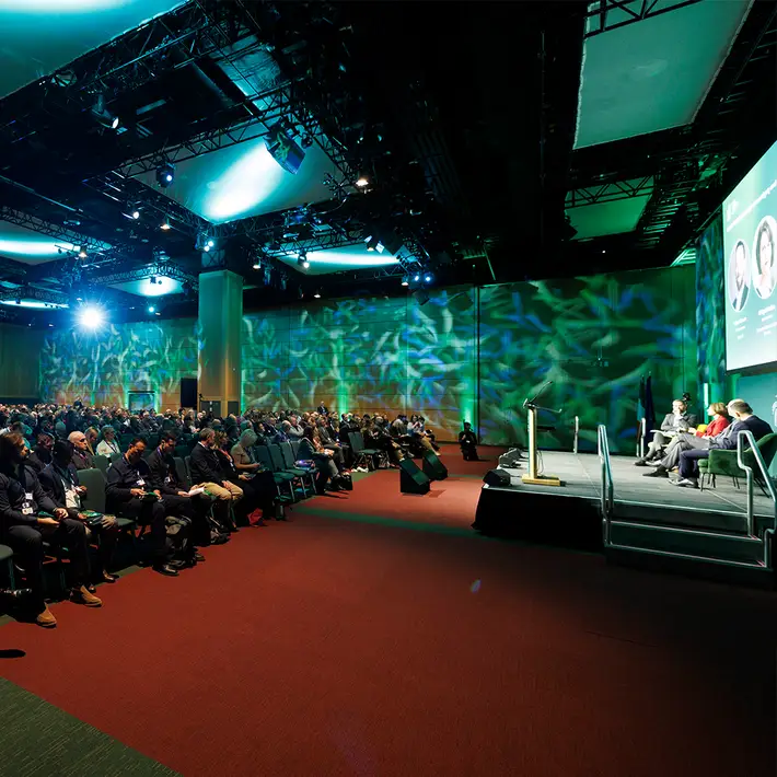 Side view of the NCSC Cyber Security Conference main stage, with a panel discussion, seated delegates and green event lighting.