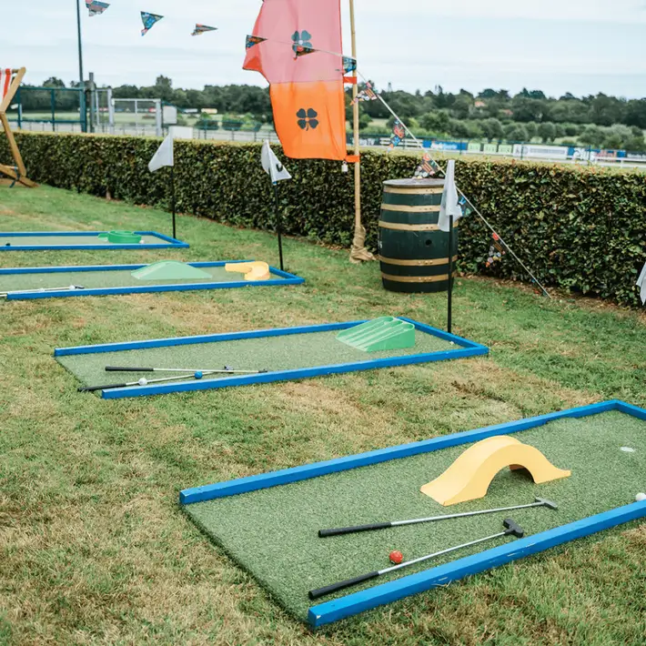 Staff playing mini golf on grass at festival-style event