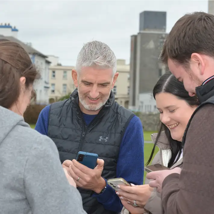 Colleagues smiling and working together on phones during a Digital Treasure Hunt team building event in Galway