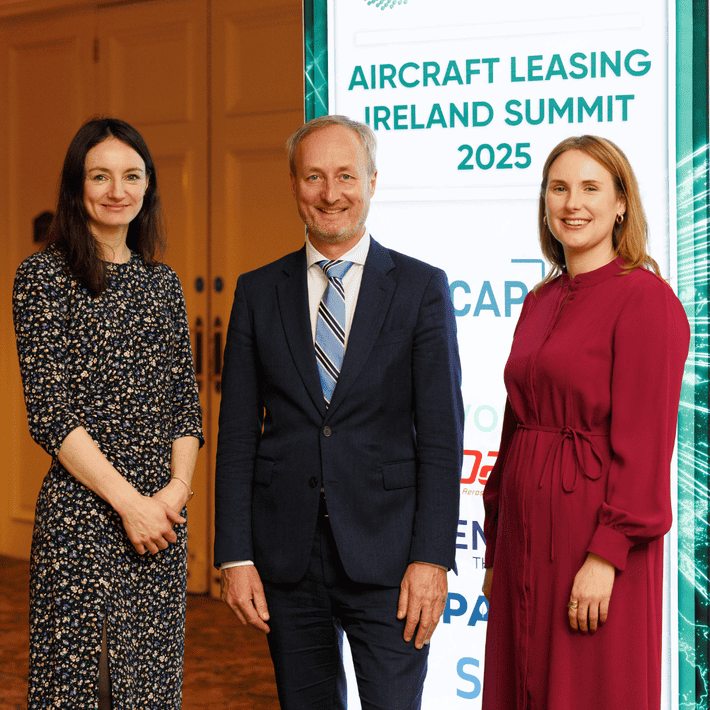 Three people posing for a picture with the backdrop of the ALI poster