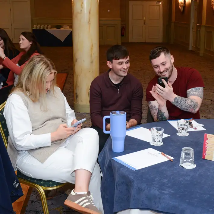 Team sitting together at a table reviewing treasure hunt photos and videos on their phones during a team building event