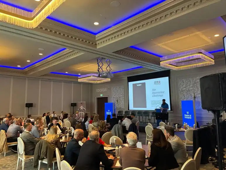 Niall briefing a detour group in a room with high ceilings and the briefing on a big screen behind Niall | Team Training Belfast