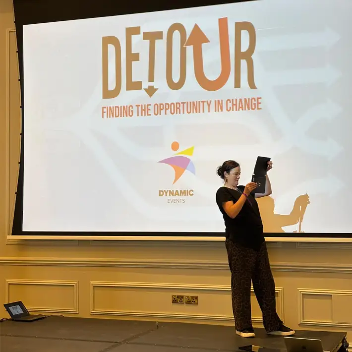 Participant completing a photo challenge on stage during the Detour change management training event at The Johnstown Estate.