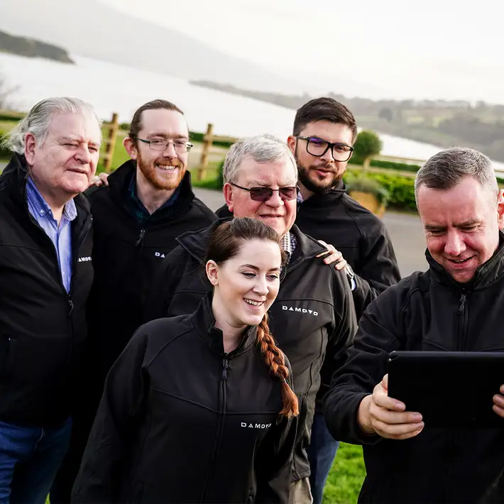 Corporate team smiling and taking a group selfie with a tablet during a Digital Treasure Hunt team building event by a lakeside venue in Ireland.