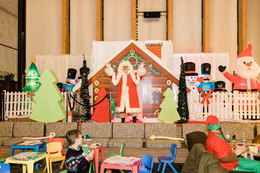 Santa Claus leading a Christmas team building event from a festive grotto stage surrounded by decorations, ideal for corporate staff parties.
