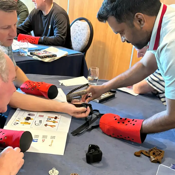 Corporate team members wearing red sleeves to assemble prosthetic hands during The Hand Project CSR team building activity, highlighting teamwork and empathy
