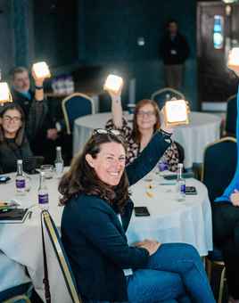 Indoor team building activity with corporate employees holding up solarbuddy lights at round tables during a facilitated team buildingworkshop in Dublin.