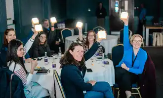 Indoor team building activity with corporate employees holding up solarbuddy lights at round tables during a facilitated team buildingworkshop in Dublin.