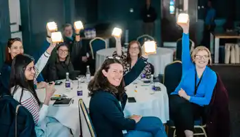 Indoor team building activity with corporate employees holding up solarbuddy lights at round tables during a facilitated team buildingworkshop in Dublin.