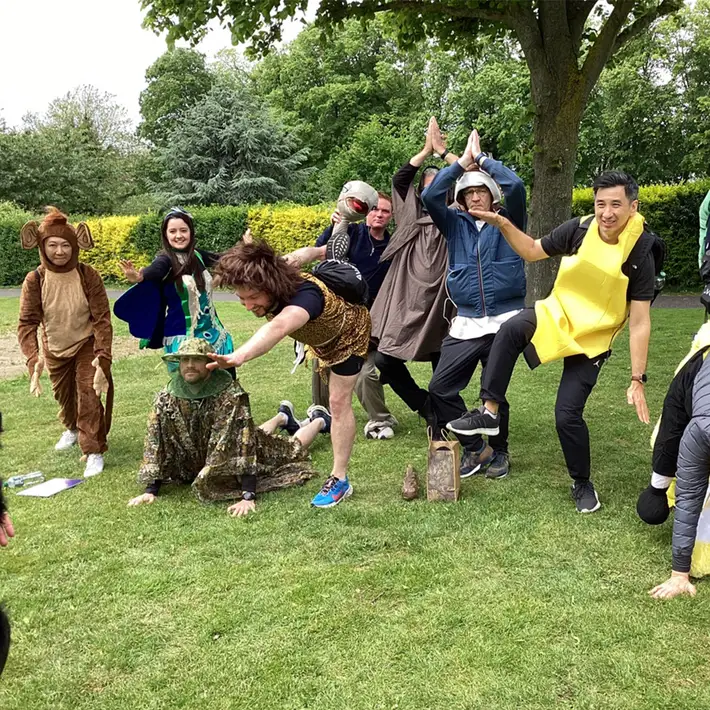 Participants in creative jungle-inspired costumes, including a lion, a snake, and an owl, forming a united pose as they take on the survival challenge together. Their expressions reflect excitement and adventure.