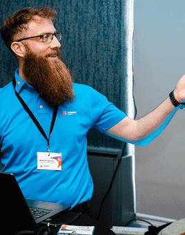 Facilitator leading a corporate team development session, smiling and engaging with participants at a workshop, wearing a Dynamic Events shirt.