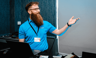 Facilitator leading a corporate team development session, smiling and engaging with participants at a workshop, wearing a Dynamic Events shirt.
