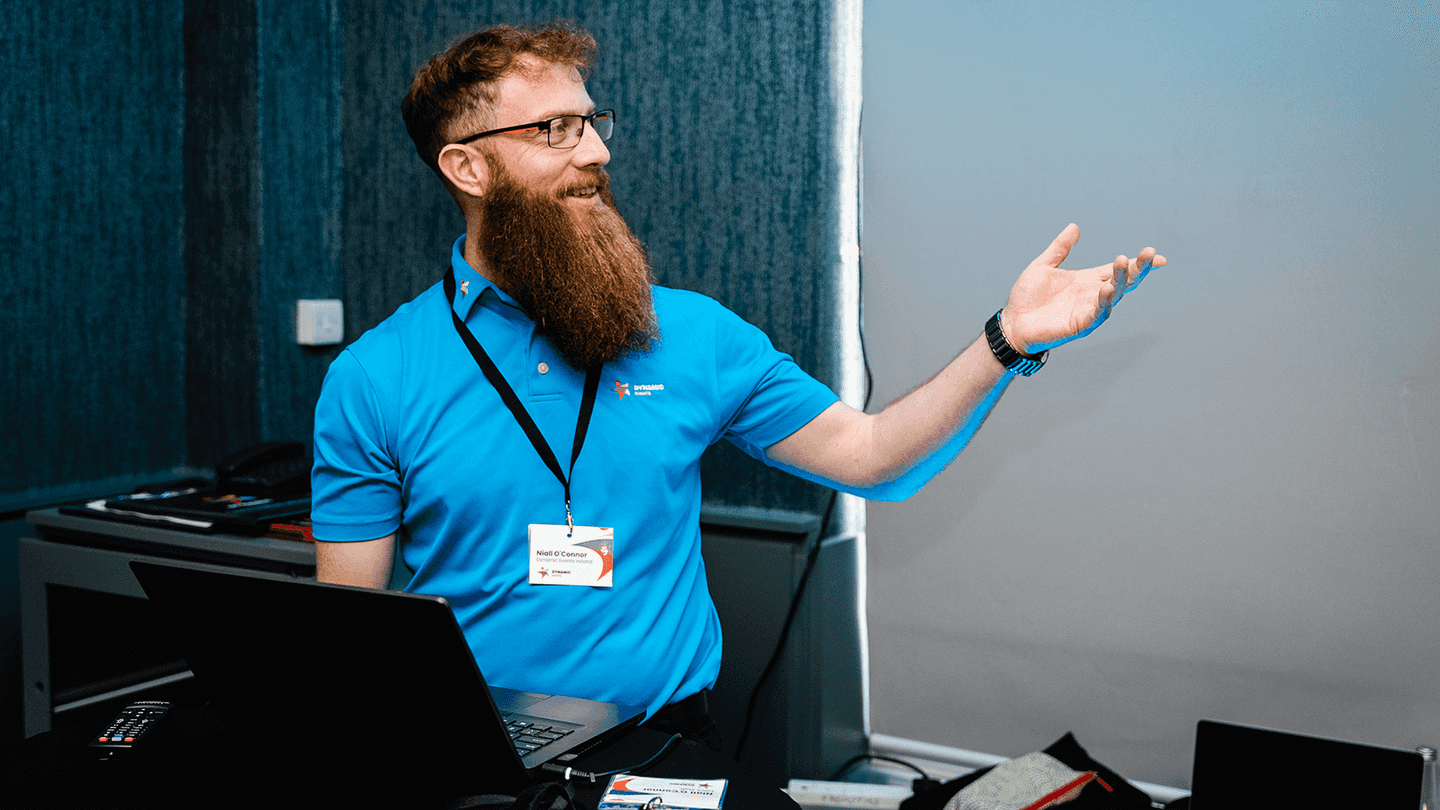 Facilitator leading a corporate team development session, smiling and engaging with participants at a workshop, wearing a Dynamic Events shirt.