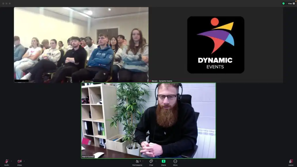 Remote host facilitating a hybrid team building activity while an in-person team listens on screen.