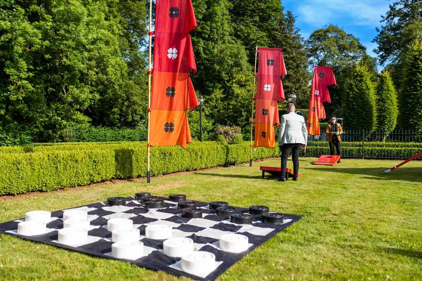 Giant checkers board and cornhole set up on manicured lawn for corporate summer team building