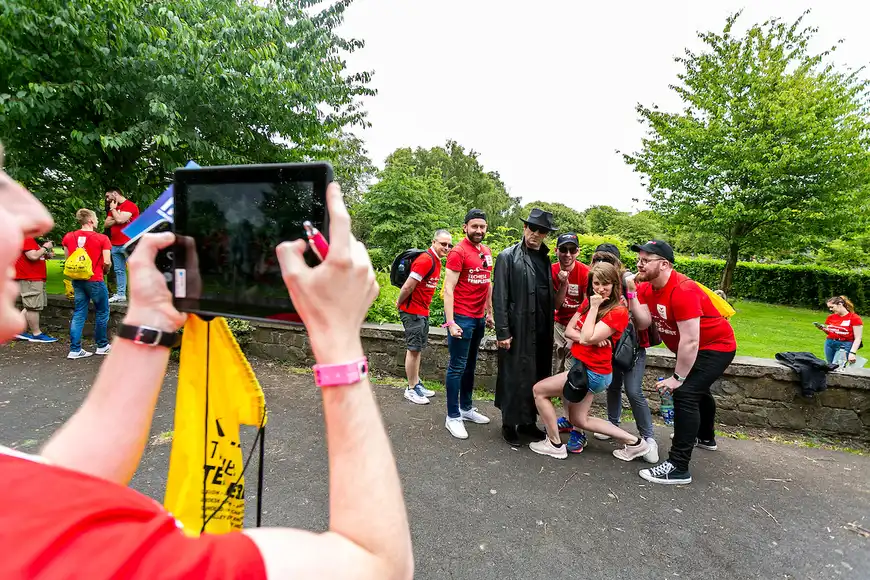 Corporate team posing with a villain character during a themed murder mystery task in a park