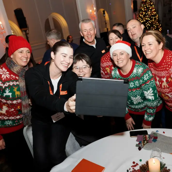 Office team enjoying a Christmas treasure hunt activity in Ireland, taking a group selfie with an iPad during a festive team building event.