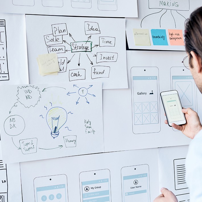 Rear view of brown-haired man testing new app on smartphone while working on interface design in office