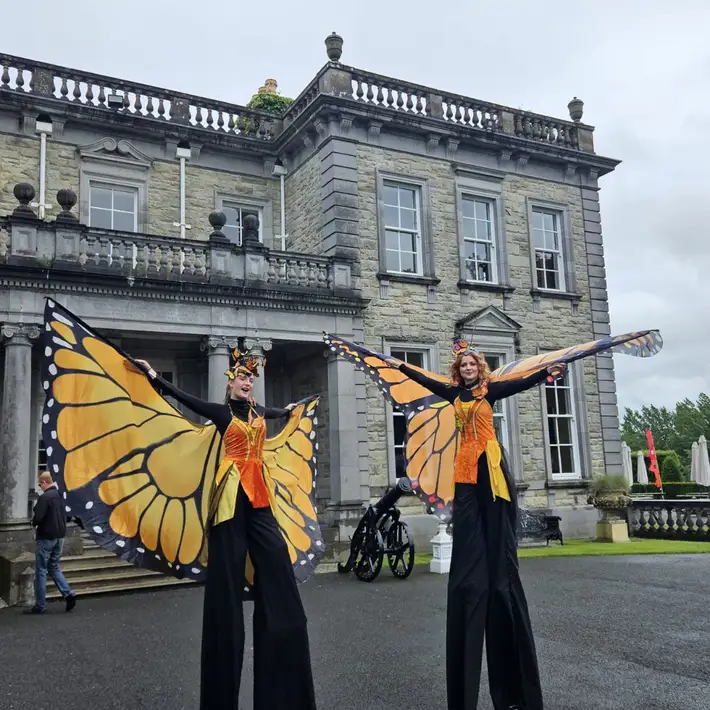 Two stilt walkers dressed as butterflies greeting families at the welcome archway entrance