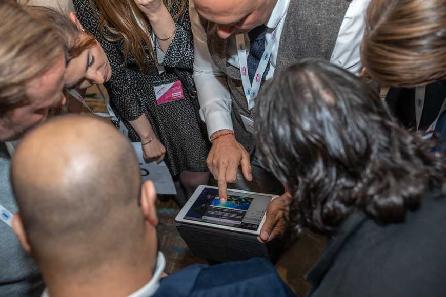 Team crowding around an iPad to solve a question during interactive digital quiz challenge