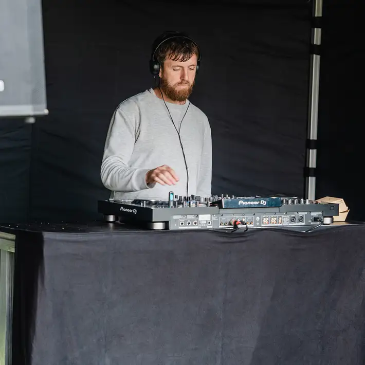 DJ performing under marquee with dancing crowd during evening set