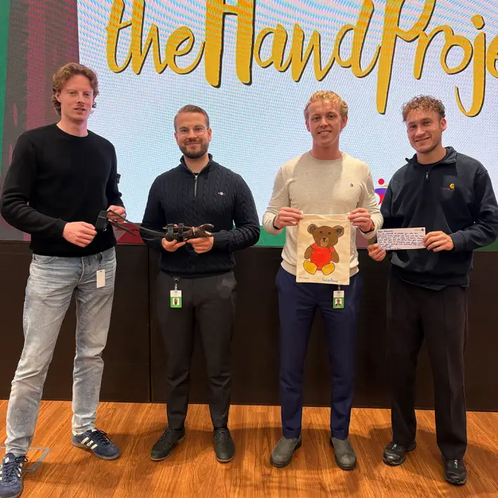 Corporate group showcasing their completed prosthetic hand and a decorated donation bag with teddy bear design during The Hand Project CSR team building in Ireland.