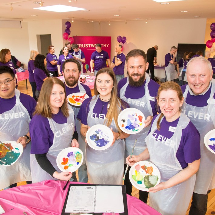 Corporate team smiling while holding painted plates during a collaborative team building activity called The Big Picture in Ireland