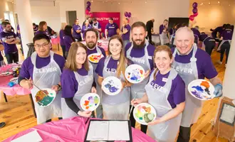 Corporate team smiling while holding painted plates during a collaborative team building activity called The Big Picture