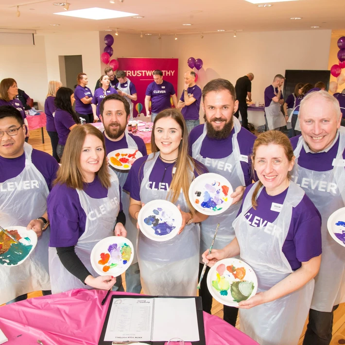 Corporate team smiling while holding painted plates during a collaborative team building activity called The Big Picture in Ireland