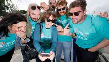 Team of six smiling and pointing at a smartphone screen during a digital treasure hunt