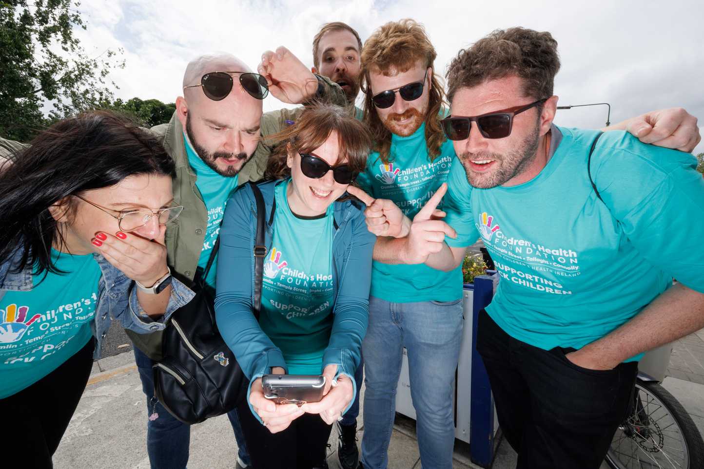 Team of six smiling and pointing at a smartphone screen during a digital treasure hunt