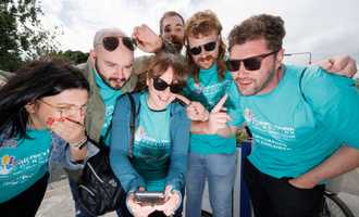 Team of six smiling and pointing at a smartphone screen during a digital treasure hunt