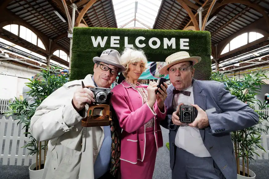 Three costumed actors posing under a Welcome sign at an indoor murder mystery corporate event