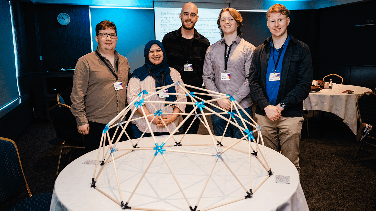 Corporate team members standing around a completed dome structure during a Dome Works team development workshop in Dublin, smiling after successfully completing a collaborative construction challenge.