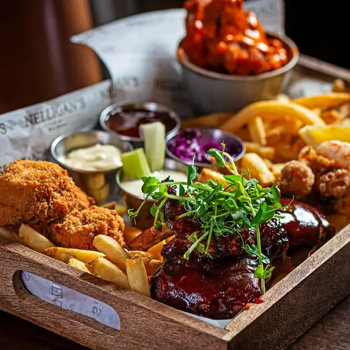A wooden tray filled with a variety of delicious foods, including BBQ ribs, crispy fries, breaded chicken, dipping sauces, and vibrant garnishes at Nelligan's | Plan your Corporate Team-Building at Kilmurry Lodge Hotel | Dynamic Events  