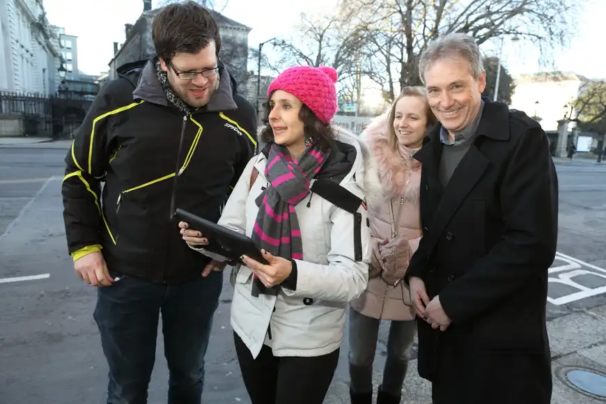 Corporate team enjoying a festive digital treasure hunt in Dublin using a tablet for interactive challenges.