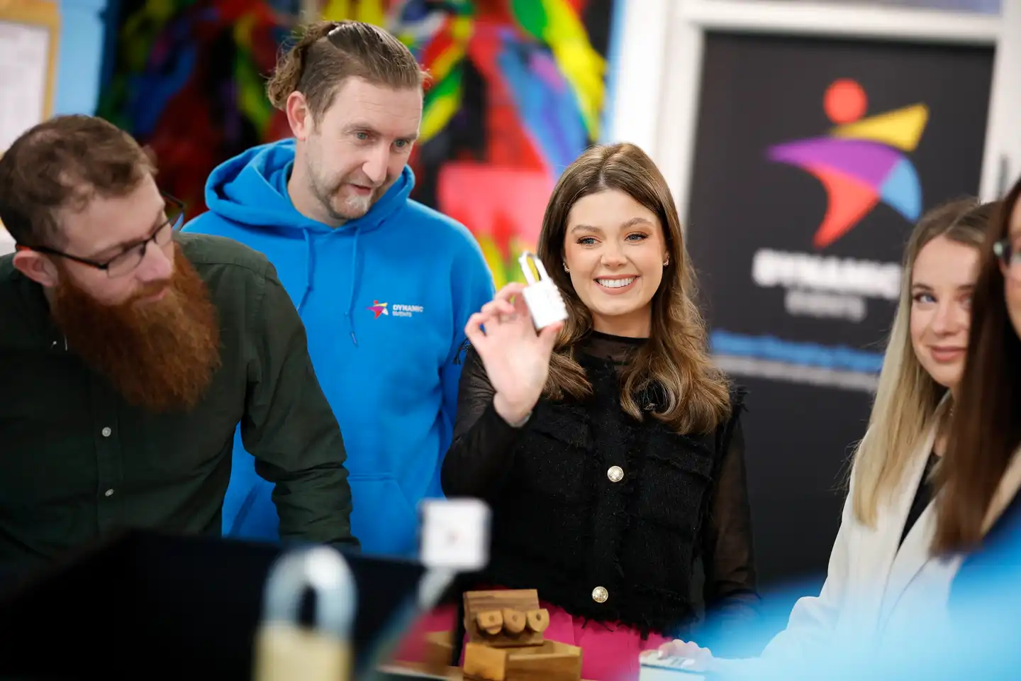 Team of colleagues solving a puzzle and smiling during an indoor Code Breaker team building activity in Ireland, with Dynamic Events branding in the background