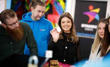 Team of colleagues solving a puzzle and smiling during an indoor Code Breaker team building activity in Ireland, with Dynamic Events branding in the background