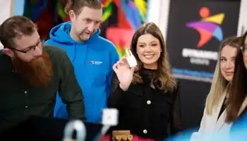 Team of colleagues solving a puzzle and smiling during an indoor Code Breaker team building activity in Ireland, with Dynamic Events branding in the background