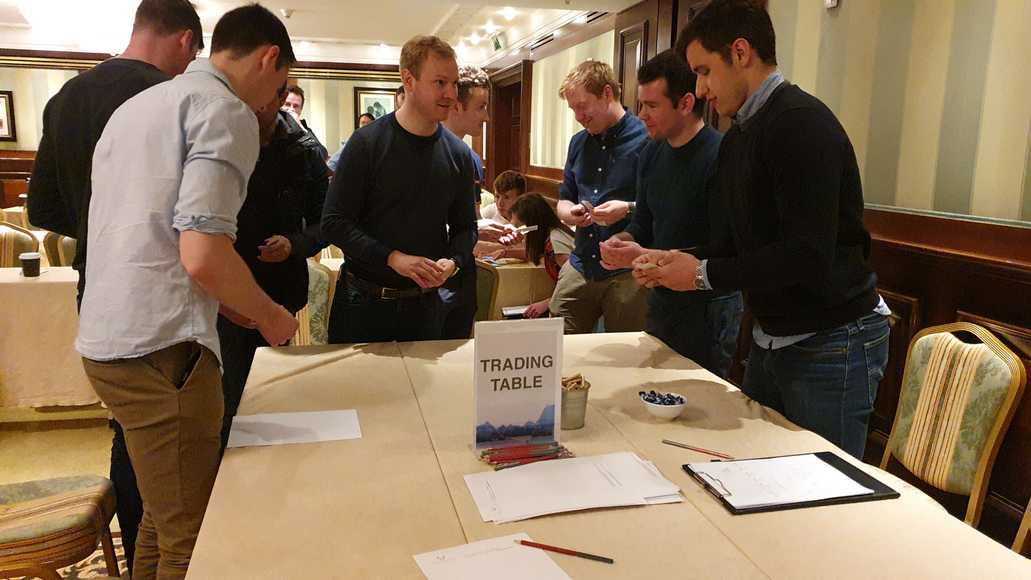 Corporate team interacting at a trading challenge table during a collaboration-based team building event.