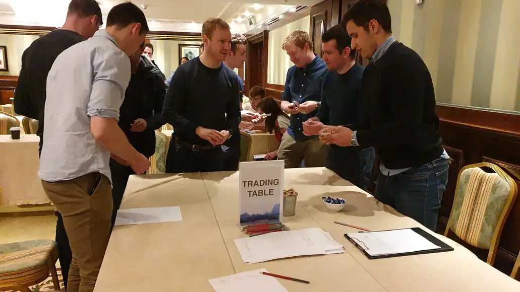 Business simulation team building participants strategising at trading table