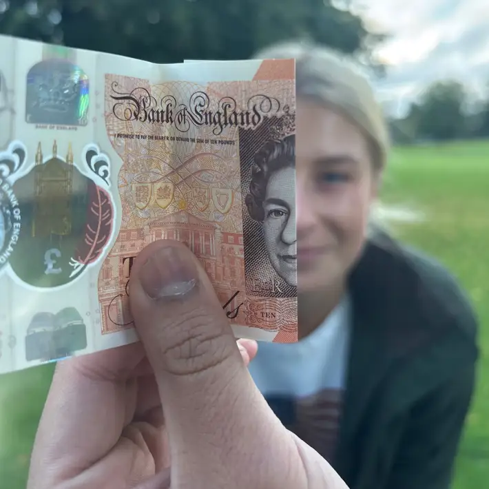 ABP Food Group graduate taking part in a digital treasure hunt photo challenge by aligning a £10 note with their face during a multi location team building event.