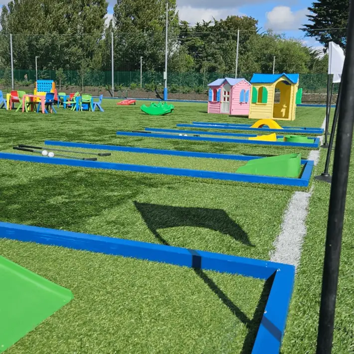 Mini golf course with toy houses in the background for a corporate family day, with blue skies and green trees