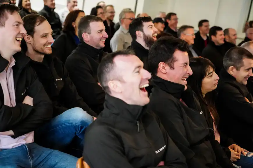 Employees laughing together while watching event highlights at a fun team building showback session.