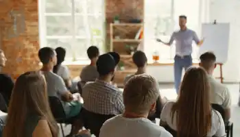 Corporate team training workshop during a company kick off meeting in Ireland, with employees listening to a facilitator presenting business goals.